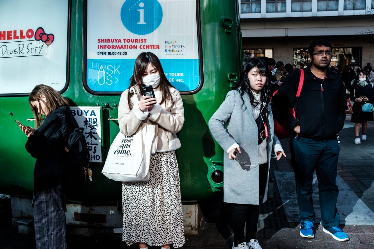 Woman in a face mask checking her phone while leaning against the Shibuya tourist information bus