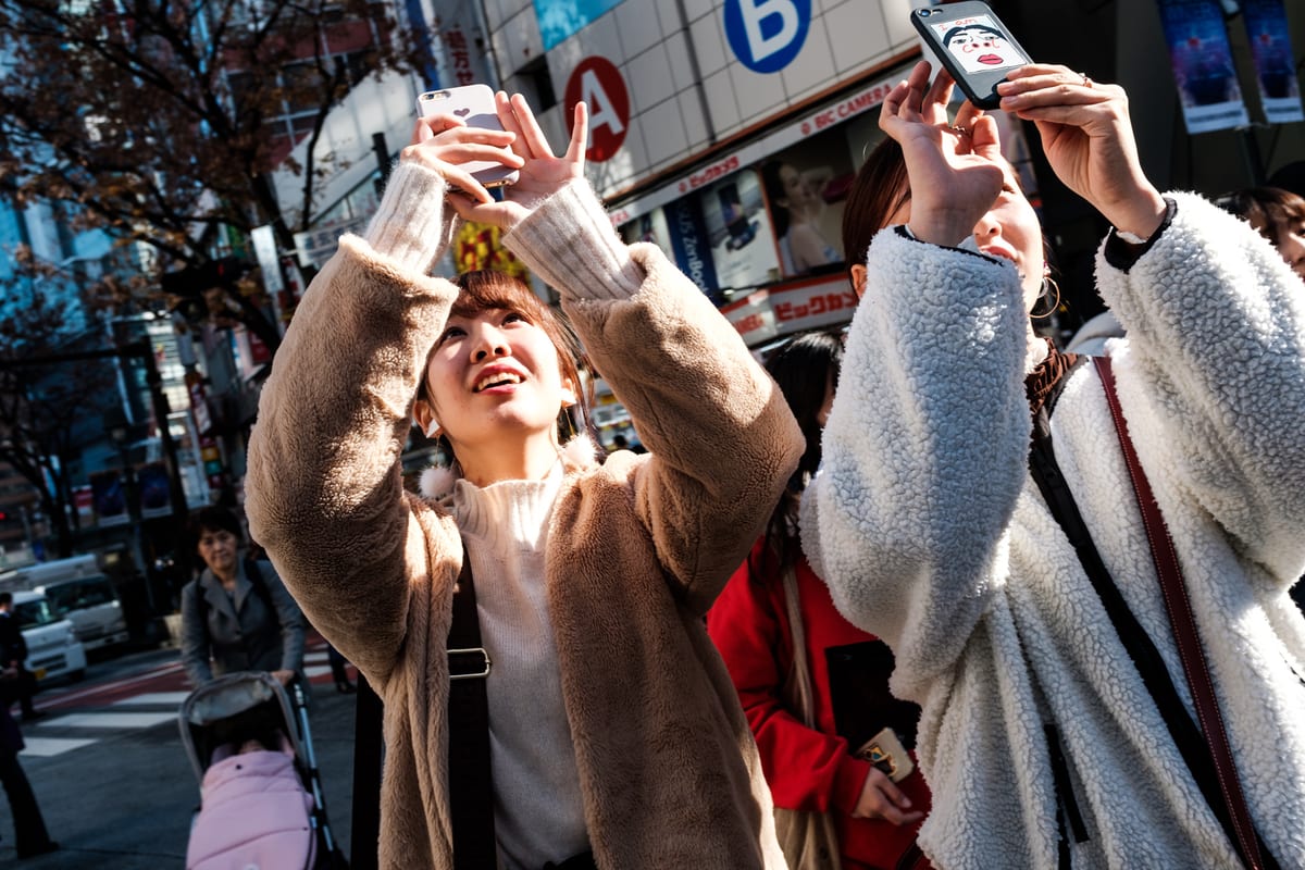 Group of young women holding up their phones to take photos on a sunlit city street