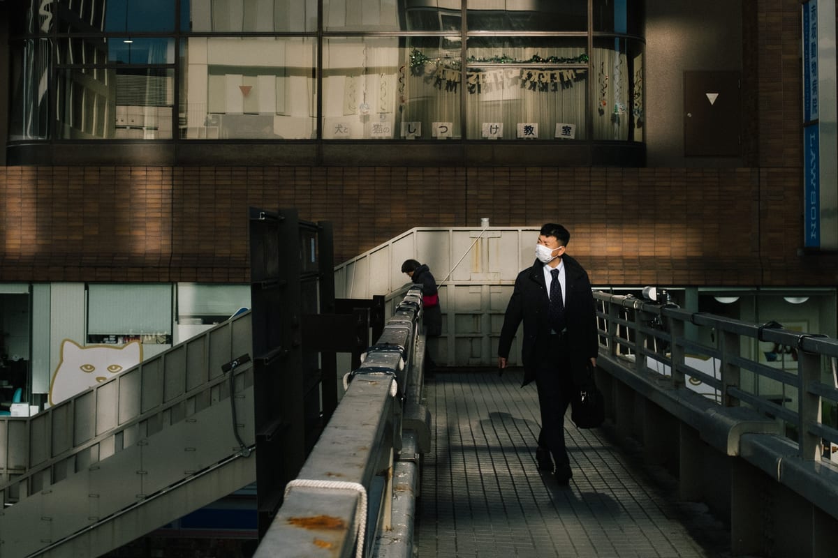 Man in a dark suit and face mask walking alone across an elevated pedestrian walkway