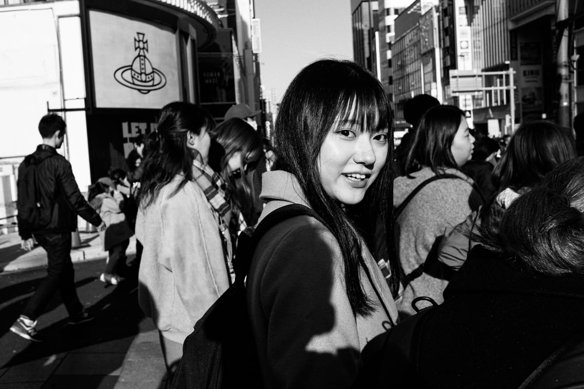 Smiling young woman with a backpack glancing back over her shoulder in a sunlit crowd near a storefront