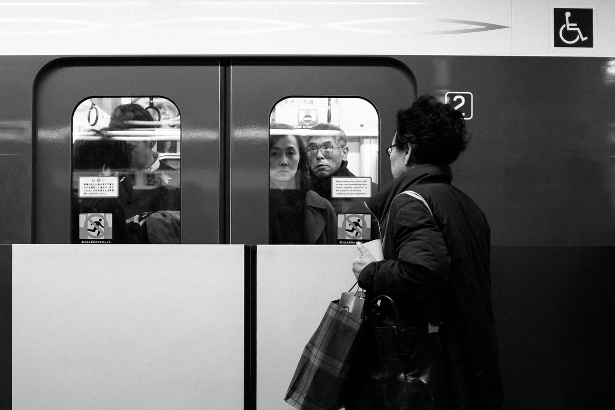 Woman holding shopping bags on a subway platform as passengers peer through closed train doors
