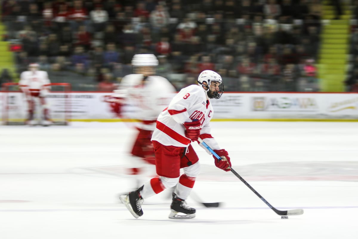 Cornell player carries the puck up the ice with blurred teammates and crowd in the background