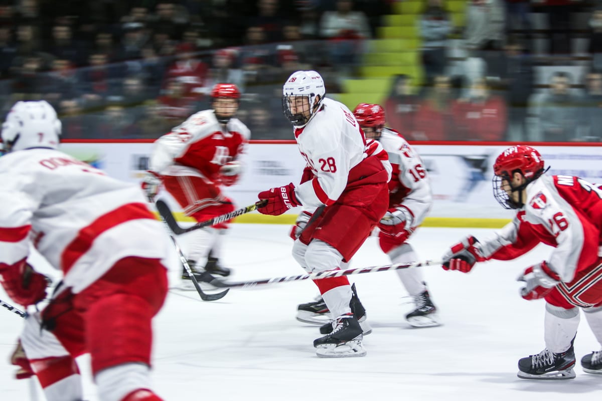 Cornell player looks up ice surrounded by players from both teams, motion blur on the surrounding figures