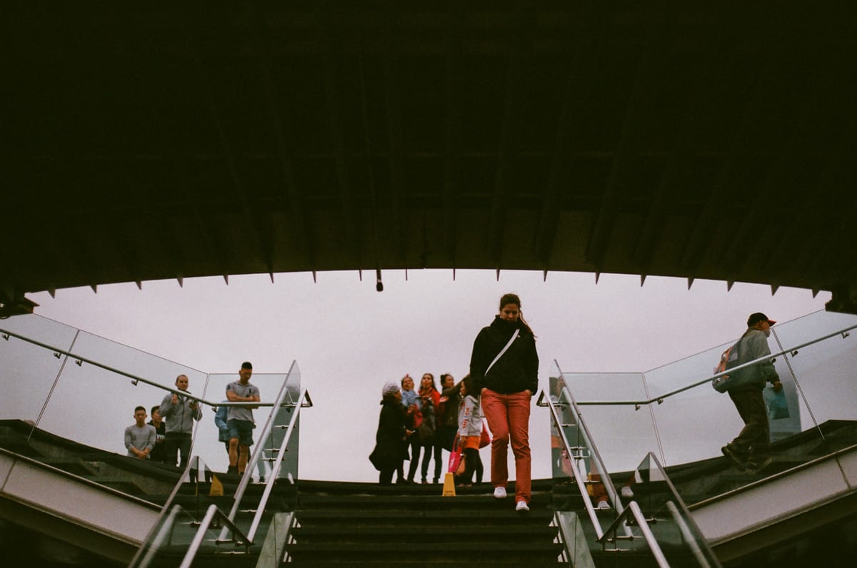 People descending a wide staircase viewed from below, framed by a dark architectural overhang