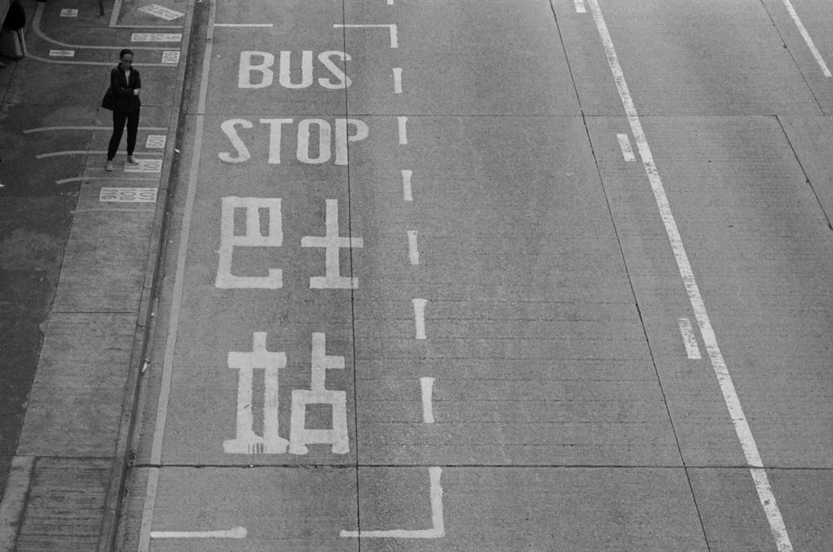 Overhead view of a road with BUS STOP painted in English and Chinese, a lone figure in a suit standing at the curb