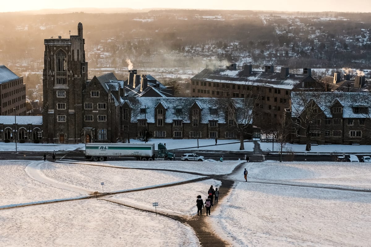 Snow-covered university campus at golden hour with figures walking along cleared paths between stone buildings