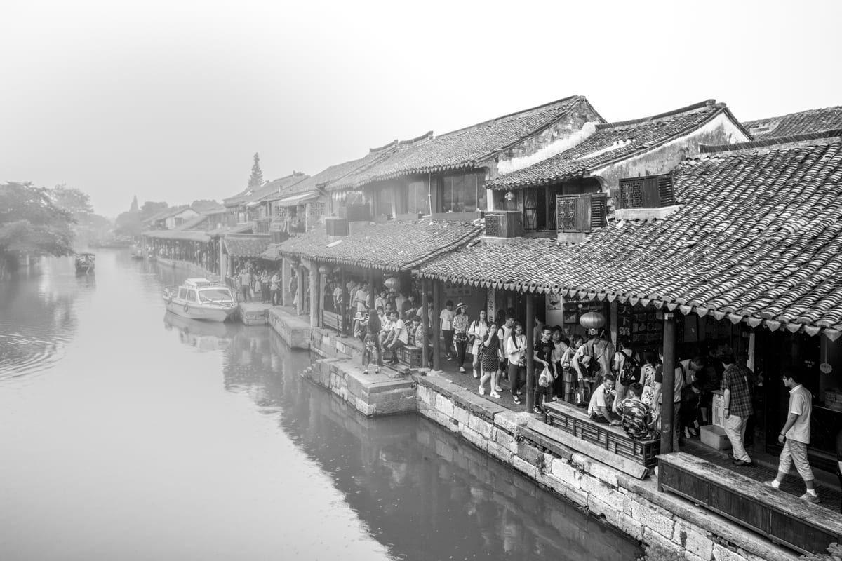A Chinese water town canal lined with crowded traditional tile-roofed shops and a boat on the water